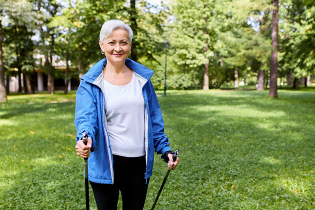 背包穿着运动服的快乐白发成年女性 享受着健康促进的体育活动 使用行走杆 有着兴奋愉悦的面部表情 呼吸着大自然中的新鲜空气 微笑着老年人活跃活力