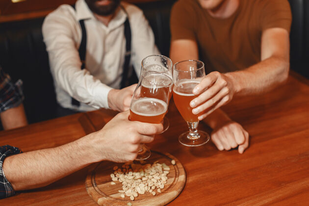 餐厅和最好的朋友见面三个穿着休闲服的快乐的年轻人一起坐在酒吧里聊天喝啤酒晚上夜生活足球