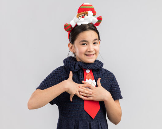 新年小女孩穿着针织连衣裙 头上系着一条红色领带 头上戴着一个有趣的圣诞戒指 手放在胸前 心怀感激领带搞笑年