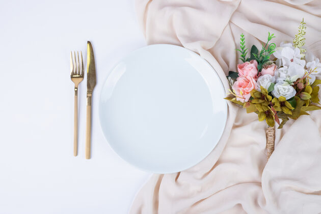 餐具白色表面上有一束鲜花 盘子和餐具盘子人造的植物