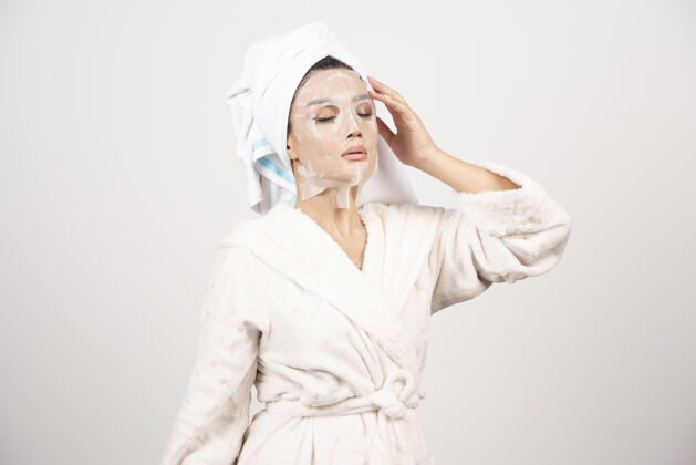 年轻穿着浴衣 头上戴着毛巾的年轻女士的肖像 同时用面罩触摸她的脸肖像皮肤女士