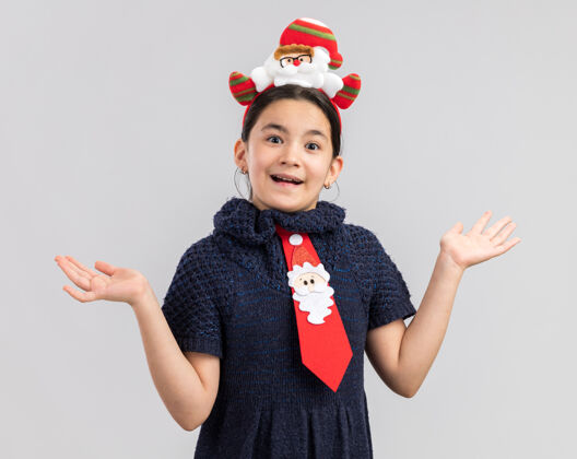 编织小女孩穿着针织连衣裙 头上系着一条红色领带 头上戴着一个有趣的圣诞戒指 看起来很高兴 兴奋地向两边张开双臂红色兴奋新年