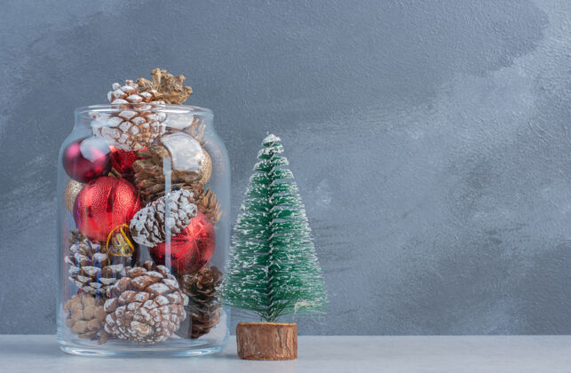 装饰一个树雕像和一个倒在地上的装满圣诞饰品的罐子在大理石表面松树装饰品树