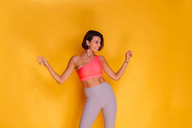 活跃年轻健壮的女人穿着运动服 时髦的上衣和紧身裤 对着黄色的墙壁摆姿势年轻服装运动