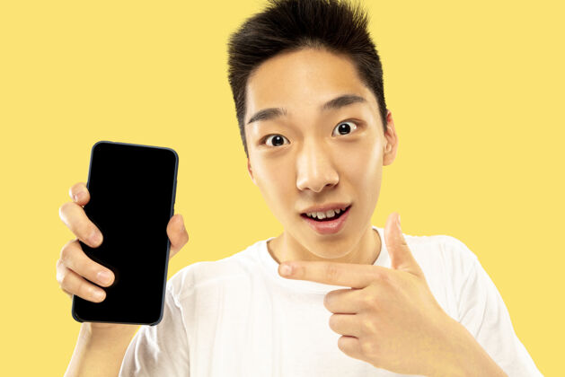 人韩国年轻人的肖像穿白衬衫的男模使用智能手机下注 看新闻或聊天人类情感的概念 面部表情成人男人肖像