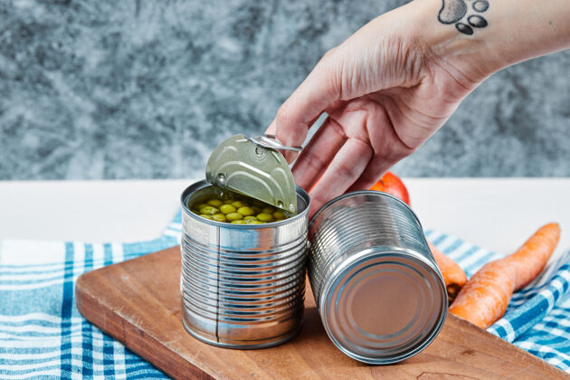 食物手拿一罐煮青豌豆放在一张白色的桌子上 桌子上放着蔬菜和桌布小吃堆锡