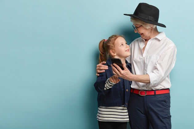 信息有趣的积极的老妇人拥抱小孙女 在现代手机上拍照 自拍的乐趣 互相看看 使用技术家庭 生活方式和关系的概念成熟女儿积极