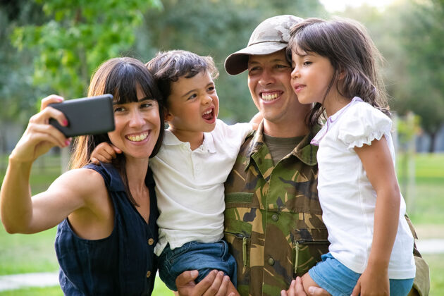中镜头快乐快乐的军人家庭庆祝爸爸归来 在公园里享受休闲时光 在智能手机上自拍中镜头家庭团聚或回家的概念手机智能手机白种人