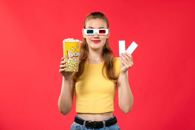年轻的前视图年轻女性在电影院拿着爆米花包和电影票在淡红墙影院电影票浅红色