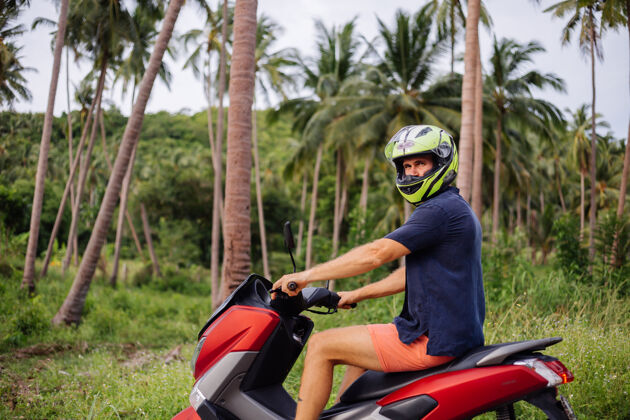 时尚在热带丛林的田野上纹着红色摩托车的壮汉控制乘坐度假