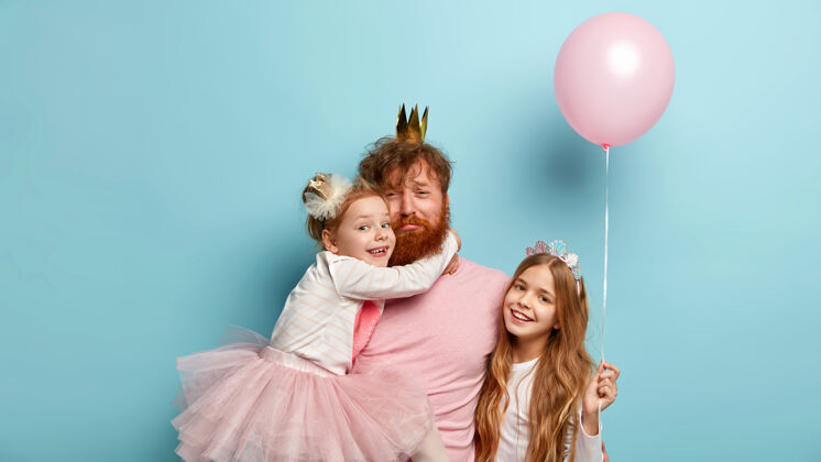 拥抱疲惫悲伤的单身父亲为孩子们组织真正的节日 戴着皇冠 接受小女儿的拥抱 长发的小女孩捧着气球 开心地笑着站在附近家庭庆典气球高兴嬉戏