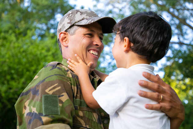 制服快乐的父亲抱着小儿子 在军旅归来后抱着男孩在户外低角度家庭团聚或回家的概念父母头发拥抱