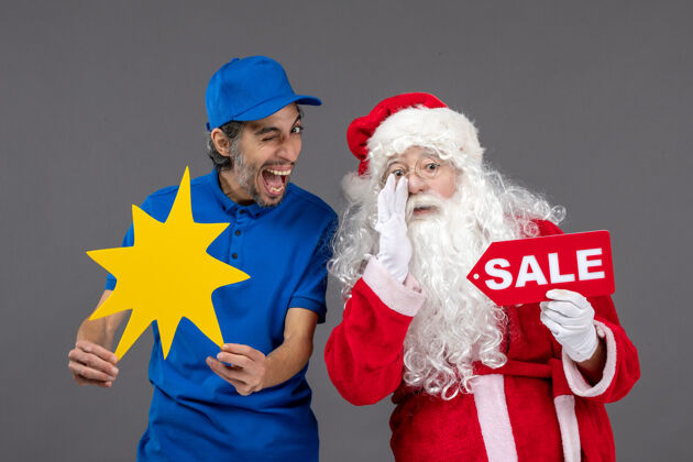 人圣诞老人的正面图 男性信使手持销售横幅 灰色墙上有黄色标志快乐工作节日