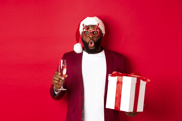 促销圣诞节戴着派对眼镜和圣诞帽的英俊的非洲裔美国人男人开朗杯子