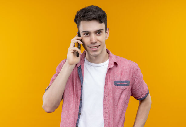穿着微笑的白人年轻人穿着粉色衬衫在孤立的橙色背景下讲电话电话小伙子橙色