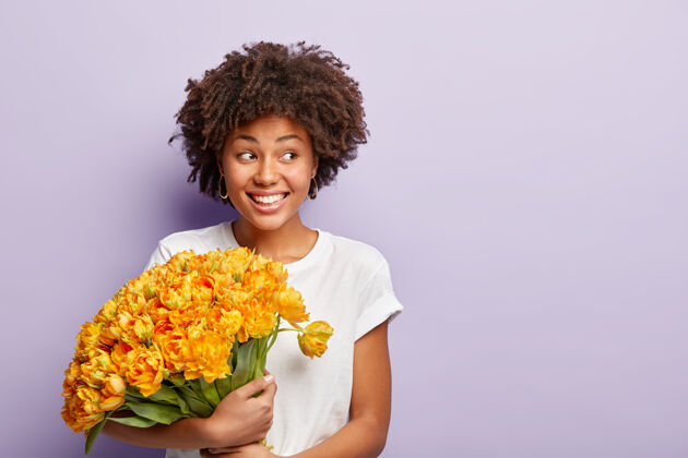 姿势生日快乐女人的形象 庆祝特别的日子 得到一大束桔黄色的花 穿着休闲t恤 专注在一边 脸上带着微笑 看着一边 会见客人 穿着休闲t恤自由空间大笑个人