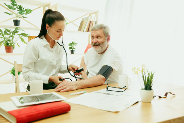 随意看护老人的来访护士或健康来访者在家里的生活方式画像医疗 保健和预防在来访期间检查或测量病人血压的女孩身份证工人卡