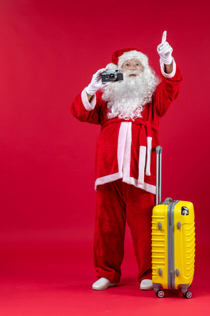 节日红墙上带黄包的圣诞老人用相机拍照的正面图圣诞老人圣诞庆祝