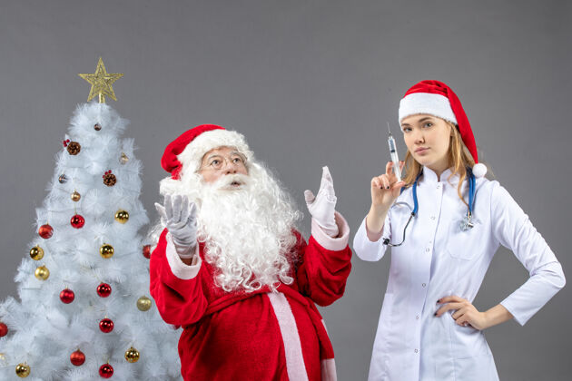 健康圣诞老人和正在灰色墙上准备注射的女医生的正视图女性圣诞快乐庆祝
