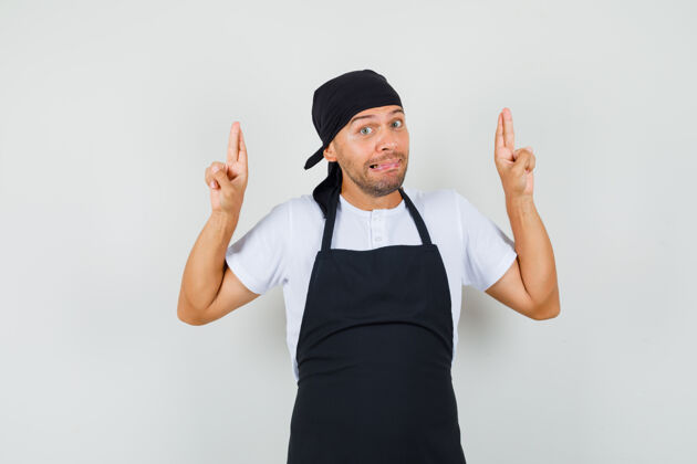 前台面包师穿着t恤 围裙 手指交叉 看起来很困惑成人厨师职业