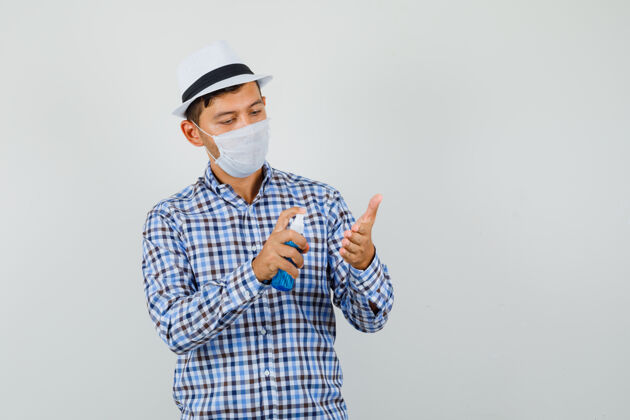 工作室穿着格子衬衫 戴着帽子 戴着口罩的年轻人 手上涂着消毒喷雾 看上去很小心成功男人开朗