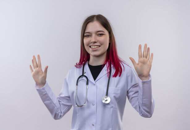 穿着微笑的年轻医生女孩穿着听诊器医用长袍 在孤立的白色背景上举手微笑提高手