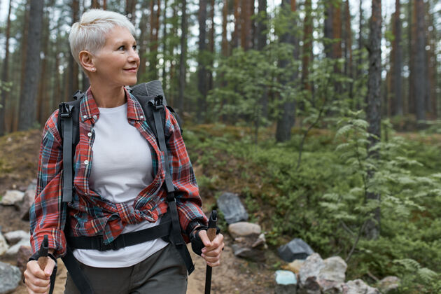 老年人快乐的欧洲女性退休者 背着背包和杆子 在松林中漫步 享受美丽的大自然自然徒步旅行老年人