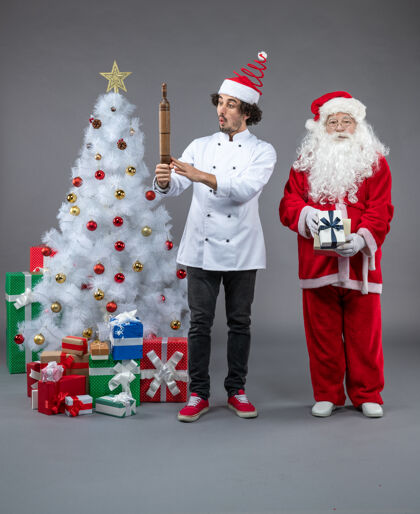 微笑圣诞老人和男厨师在灰色墙上围着圣诞礼物的正视图圣诞老人庆祝人