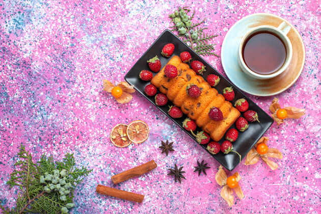 蛋糕俯瞰美味的烤蛋糕 放在黑色的蛋糕锅里 粉红色的桌子上放着新鲜的红色草莓和一杯茶水果烘焙烘焙