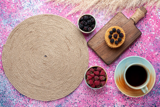书桌顶视图的小蛋糕与不同的浆果和茶杯在粉红色的表面帽檐装饰水疗