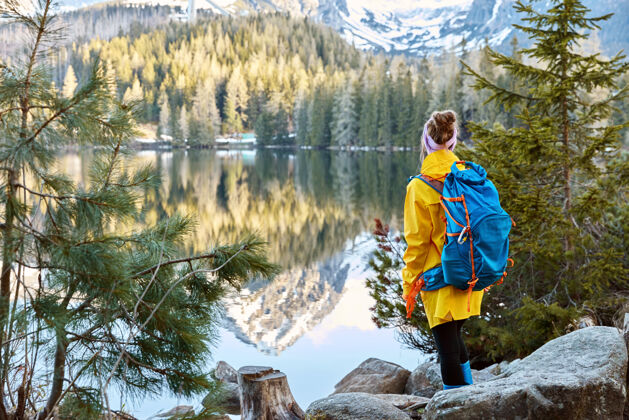 背包女游客横观静谧的远山湖景 背靠镜头自然石头欣赏