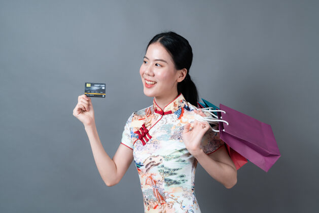 支付美丽的亚洲年轻女子穿着中国传统服饰 带着购物袋和信用卡借记买家购物者