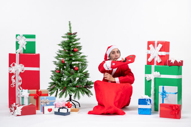 礼物新年心情与悲伤的圣诞老人坐在地上 穿圣诞袜子附近的礼物和装饰圣诞树白色背景圣诞老人坐地
