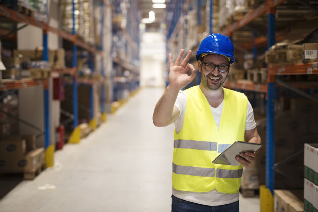 男性仓库工作人员站在大型仓储中心 在送货时表现出满意的ok手势控制积极安全