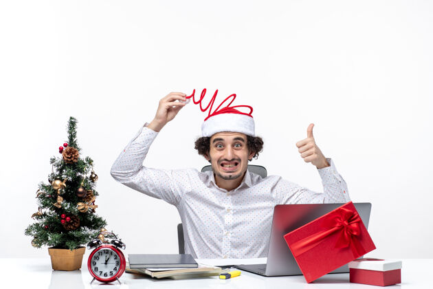 商人新年气氛与不确定的年轻商人触摸他有趣的圣诞老人帽子指着上面在白色背景的办公室人帽子办公室