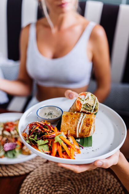 膳食在夏日咖啡厅自然采光下享用色彩缤纷的健康素食沙拉的女士美味菜肴生活方式