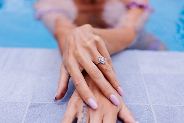 价值女士手放在游泳池边 手指上戴着戒指的特写镜头女人辉煌戒指