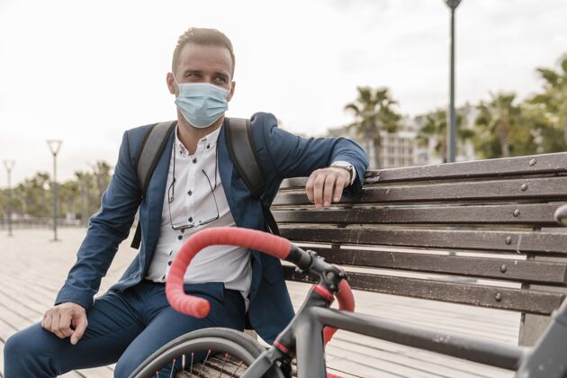 骑一个戴着口罩的男人坐在自行车旁边的长凳上积极的自行车医疗