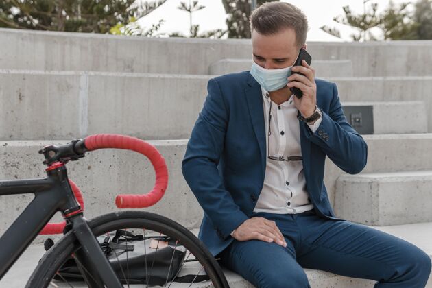 休息坐在自行车旁边戴着医用面罩的男人骑积极的医疗