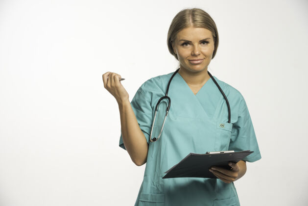 外科穿着蓝色制服的金发女医生 脖子上戴着听诊器 写着收据 思考着便条护士感染