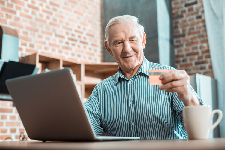 在线积极聪明的老人坐在电脑前 一边看信用卡 一边学习如何使用网上银行系统快乐技术购买