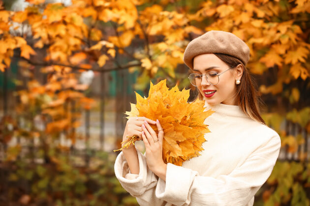 帽子秋天公园里有一位带着树叶的时髦年轻女子漂亮时尚毛衣