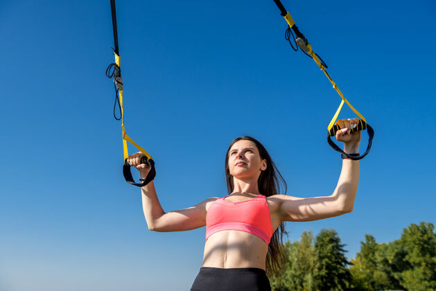 美丽在湖边的公园里 一位年轻的女士正在练习悬挂训练器训练吊索健身房