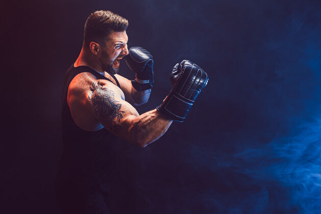 拳击留着胡须 纹身的泰拳运动员 身穿黑色汗衫 戴着拳击手套 在黑暗的墙上与烟雾搏斗运动概念意识拳击手力量