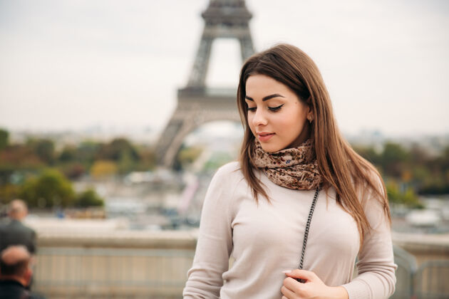 巴黎在埃菲尔铁塔的背景下 美丽的女孩向摄影师摆姿势秋天人巴黎人围巾