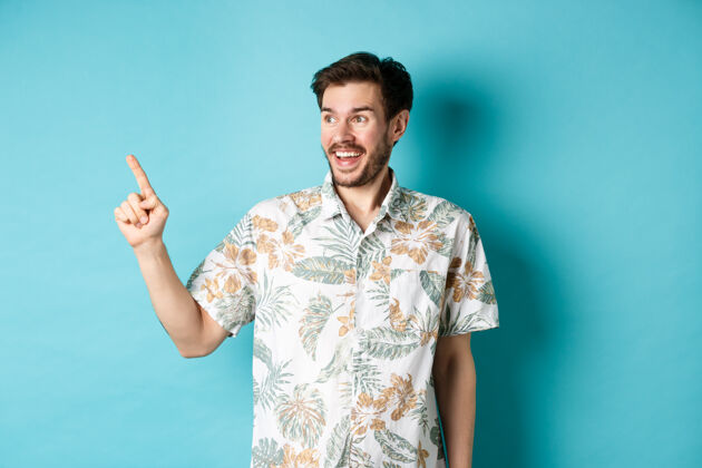 男人兴奋的游客微笑着指着空荡荡的空间 看看促销活动 穿着蓝色背景的夏威夷衬衫站在一边朋友站着酷