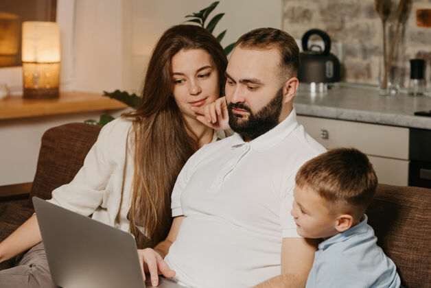 人一位留着胡子的父亲正在笔记本电脑上向儿子和家中沉思的妻子展示他的工作成就在一起电脑儿子
