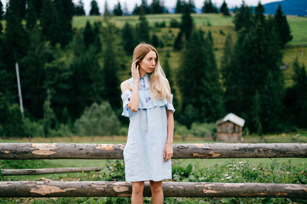乡村年轻漂亮的金发碧眼的女孩穿着蓝色的裙子在乡村的木栅栏旁摆姿势自然服饰金发