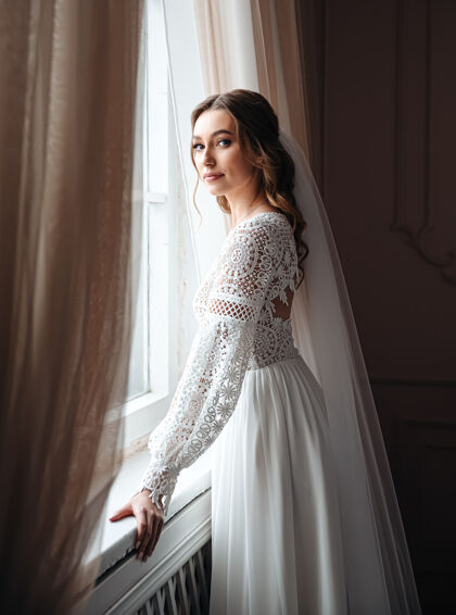 波西米亚一位穿着波西米亚蕾丝连衣裙的年轻新娘站在窗前室内婚礼女孩