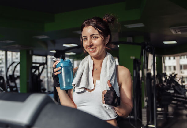 抱着一个年轻健康的女人 肩上扛着毛巾 在跑步机上拿着水瓶减肥理念 有氧运动水女人娱乐